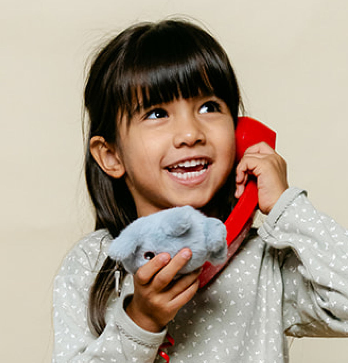 Une petite fille sourit au téléphone en tenant une peluche Hopi