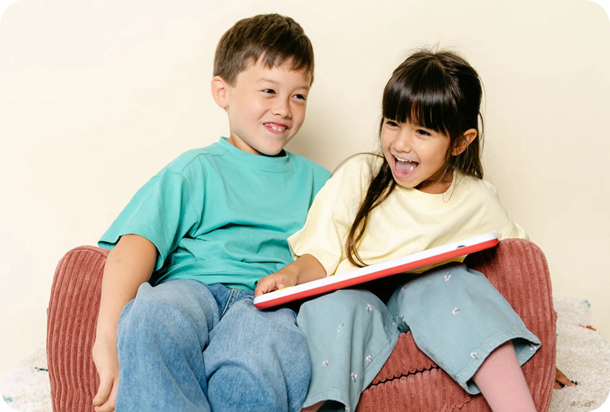 Un garçon et une fille rient sur un pouf, un livre posé sur les genoux
