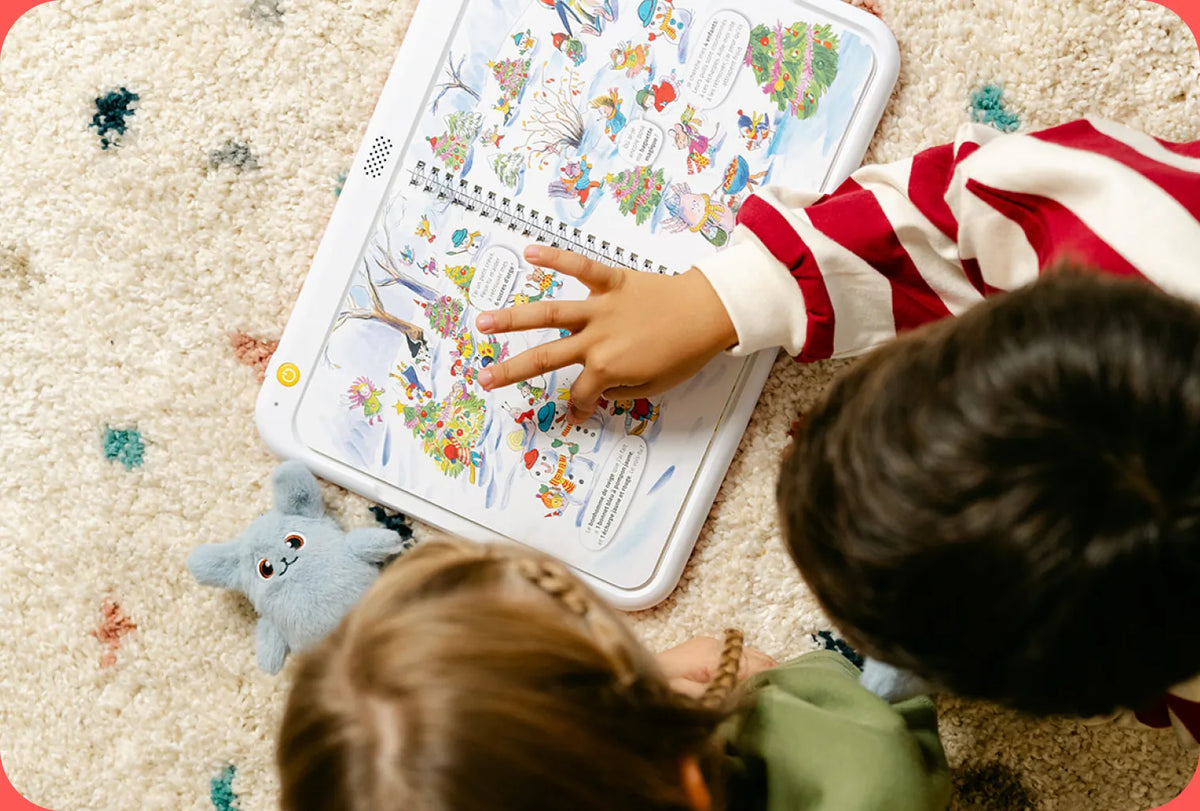 Deux enfants allongés sur un tapis touchent un livre posé sur HopiPlay
