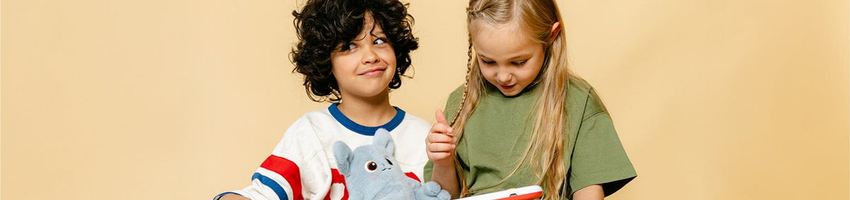Deux enfants découvrent un livre interactif avec leur peluche Hopi